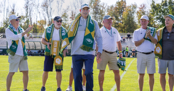 Members of the 1975 soccer team walk onto the field adorned with soccer scarves