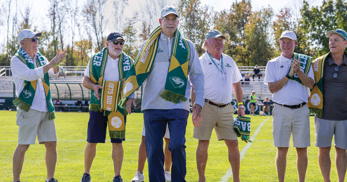 Members of the 1975 soccer team walk onto the field adorned with soccer scarves