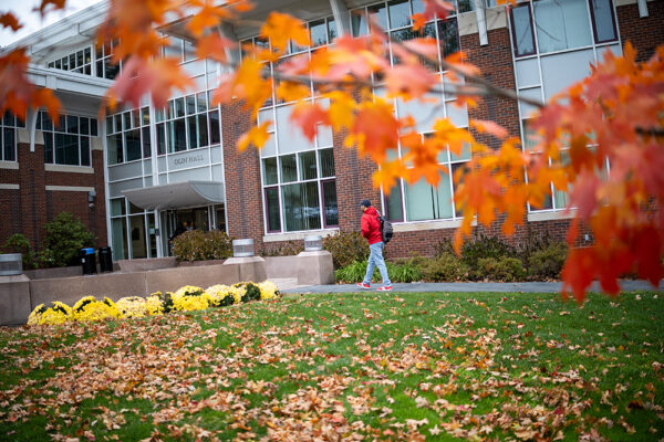 A student walks on campus amid orangish-brown foliage