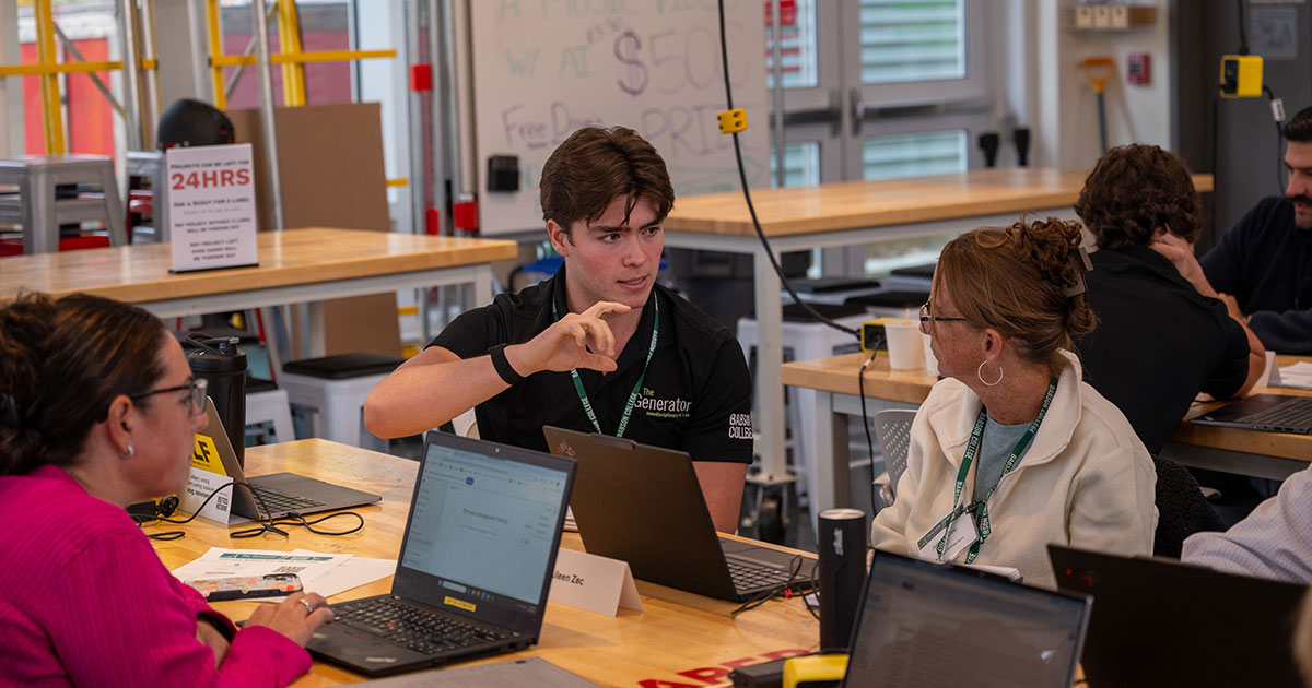 Sitting at a table, a Babson student talks with two attendees of the AI Innovators Bootcamp