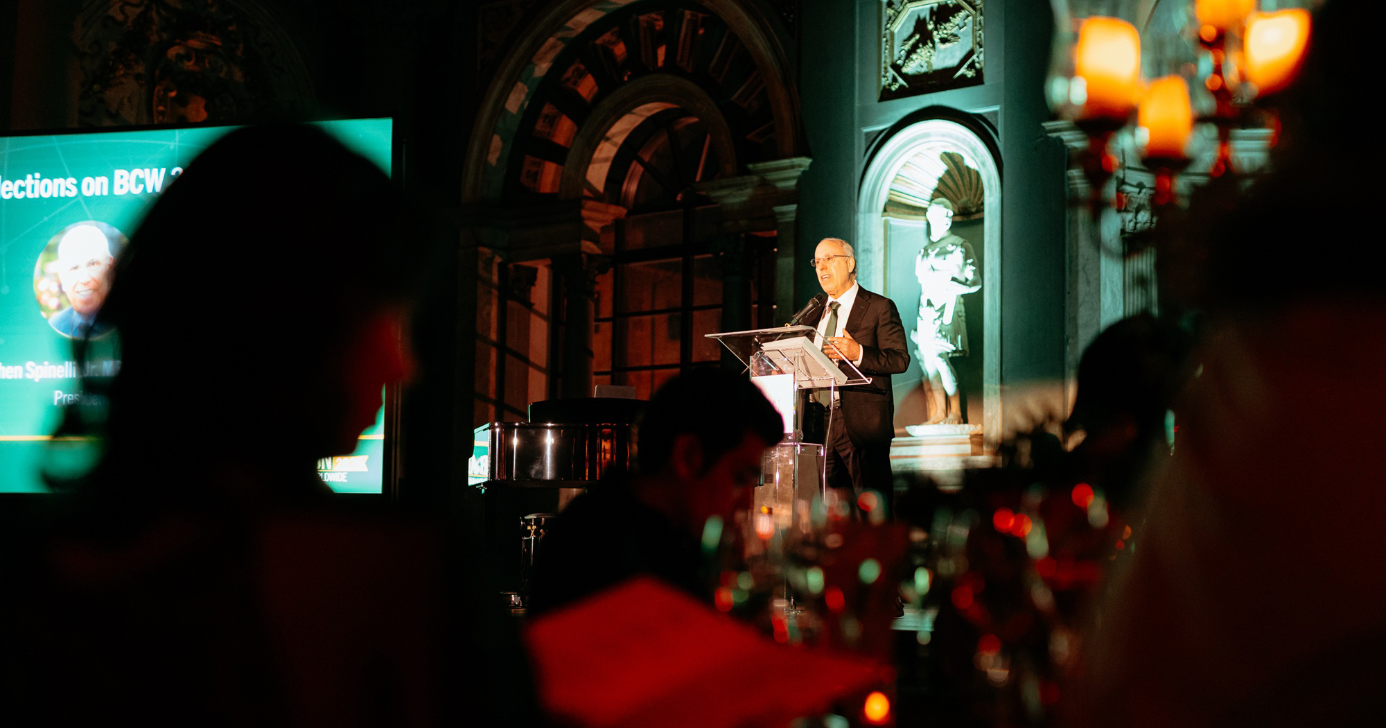 President Spinelli speaks in a dark room on stage