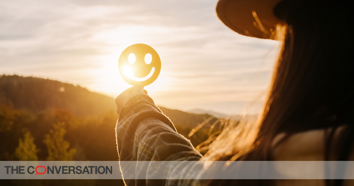 Close up of young woman holding happy smile face on background epic sunset