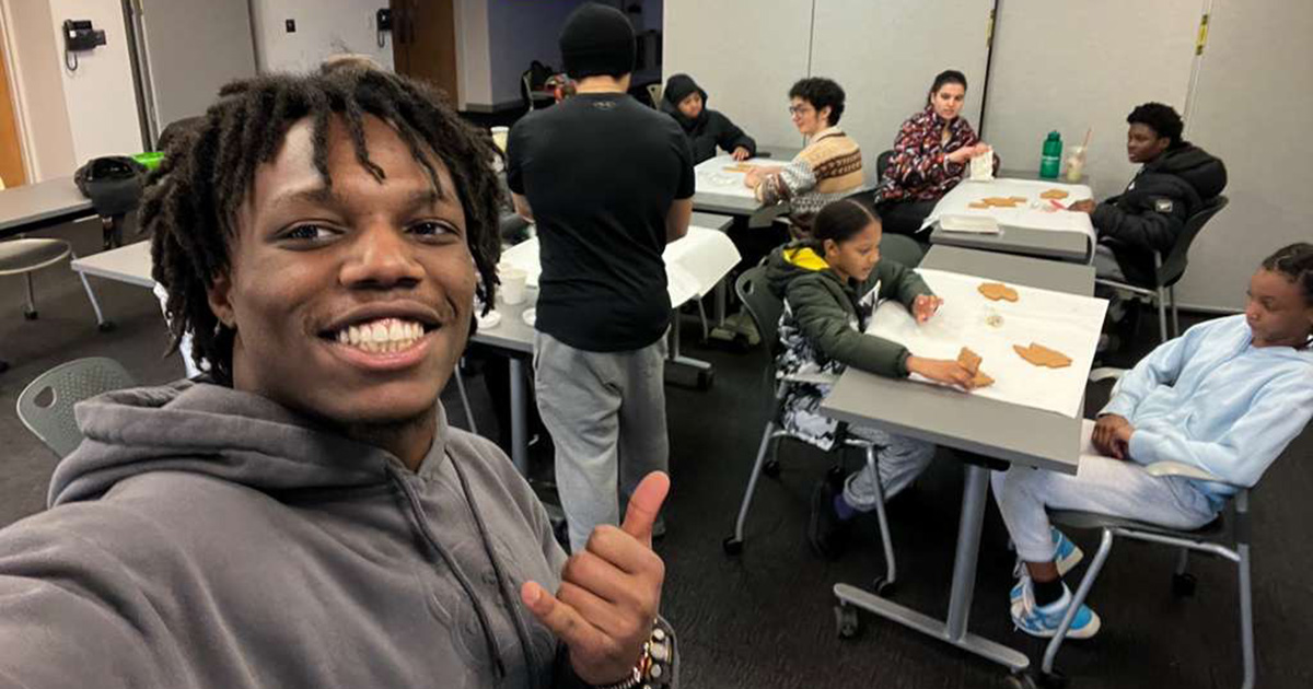 Dylan Amaswache ’27 takes a selfie with students sitting at tables behind him