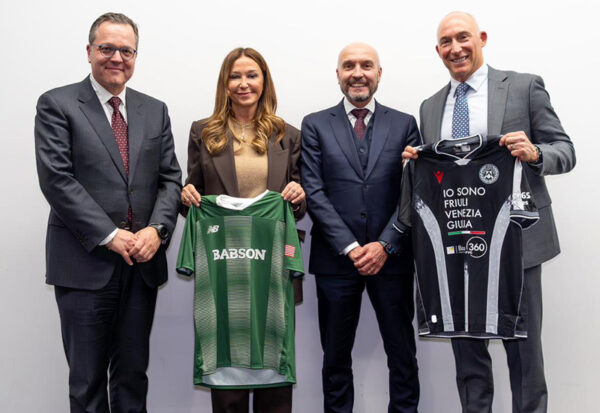 A group of four people pose for a photo, two of whom are holding up Babson and Udinese jerseys