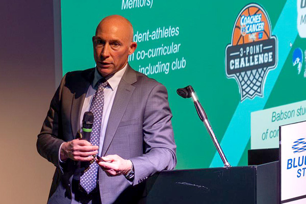 A man rests his arm on the podium while speaking during a presentation