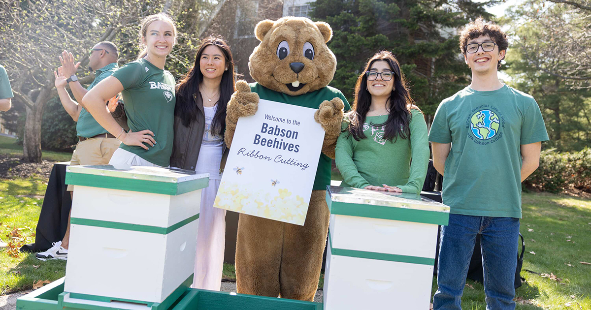 Young students stand with Beaver mascot in front of two new beehives.