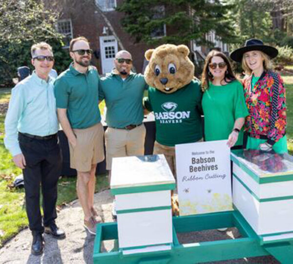 A beaver college mascot and several people stand in front of two new beehives on a sunny day.
