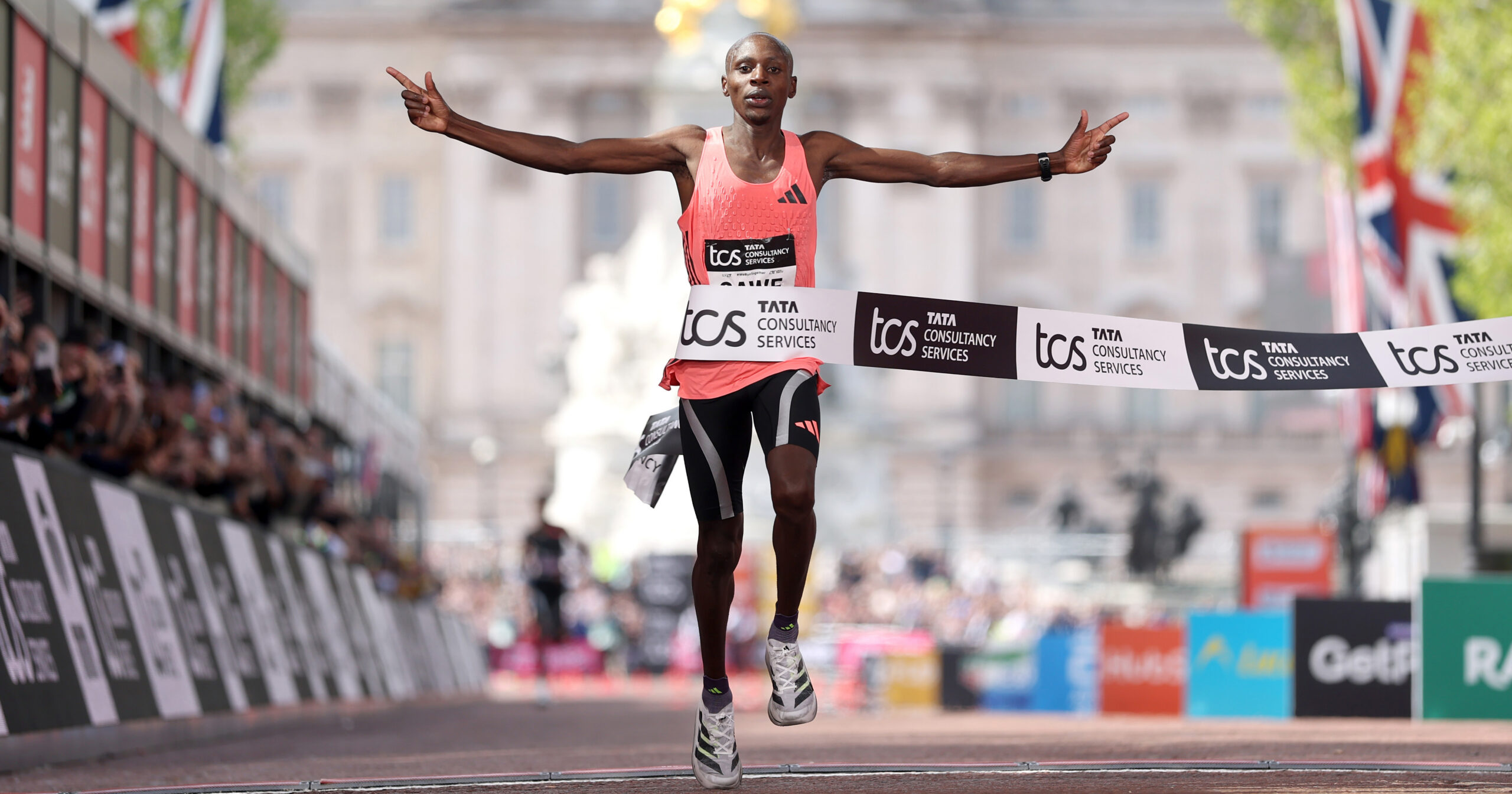 A long-distance runner crosses a marathon finish line with arms outstretched