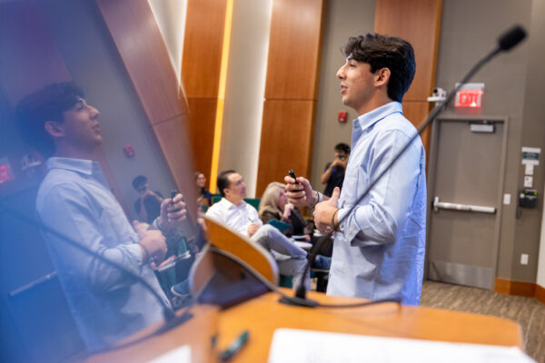 A student presenting at the B.E.T.A. Challenge is reflected in a screen on a podium