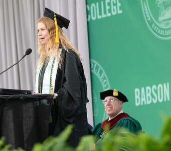Young woman speaks to fellow college graduates.
