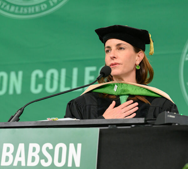 Woman speaks at lectern during graduate commencement at Babson College.