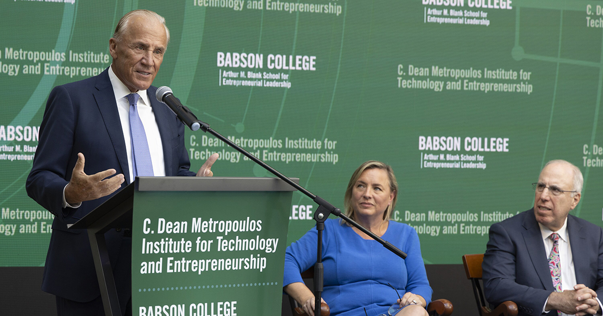 Man speaks at lectern while a woman and man look on.