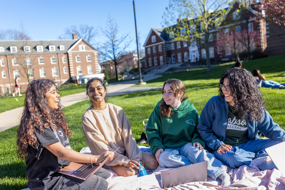 Four students sit on blanket on the Quad on a bright, sunny day