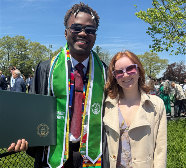A man wearing a graduation robe and woman standing on a college campus.