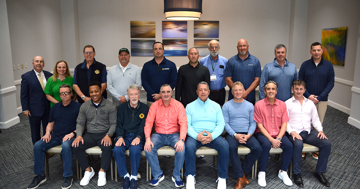 A group of 16 firefighters and a woman and man administrator from Babson College pose in a conference room during an entrepreneurial leadership program.