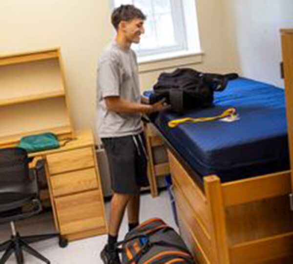 Young man unpacks in college dorm room.