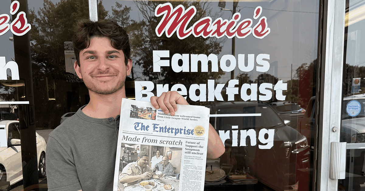 Jake Ross poses for a photo outside Maxie's Deli while holding a copy of a newspaper featuring the restaurant