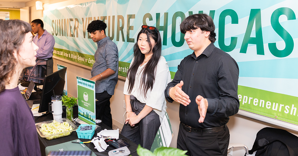 Entrepreneurs stand behind a table discussing their startups