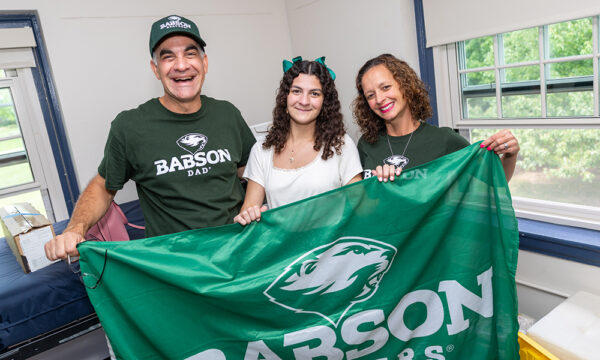 A student and her parents hold a Babson flag in her room