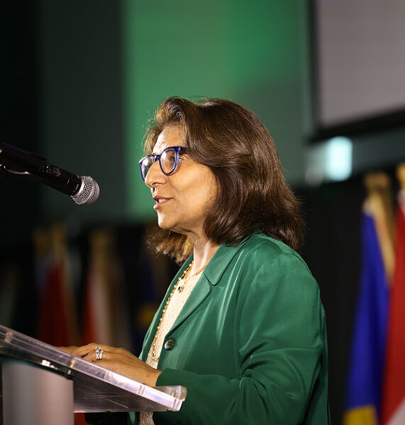 Woman wearing green blazer gives speech at lectern.