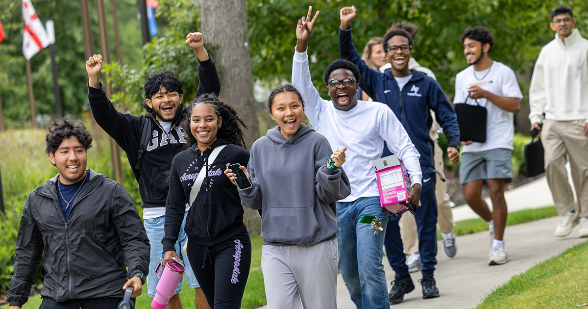 Students smile and raise their arms while walking on campus