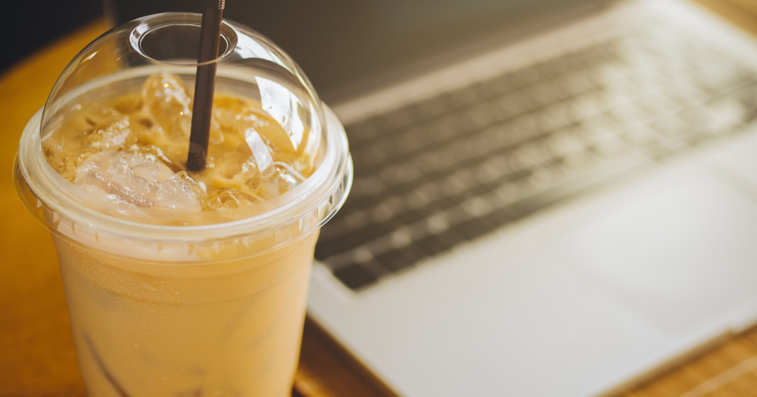 Digital and laptop computer, eyeglasses, with cup of fresh cold iced coffee on wooden table in coffee shop