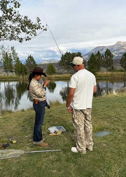 Two people stand near a lake preparing to cast while fly fishing