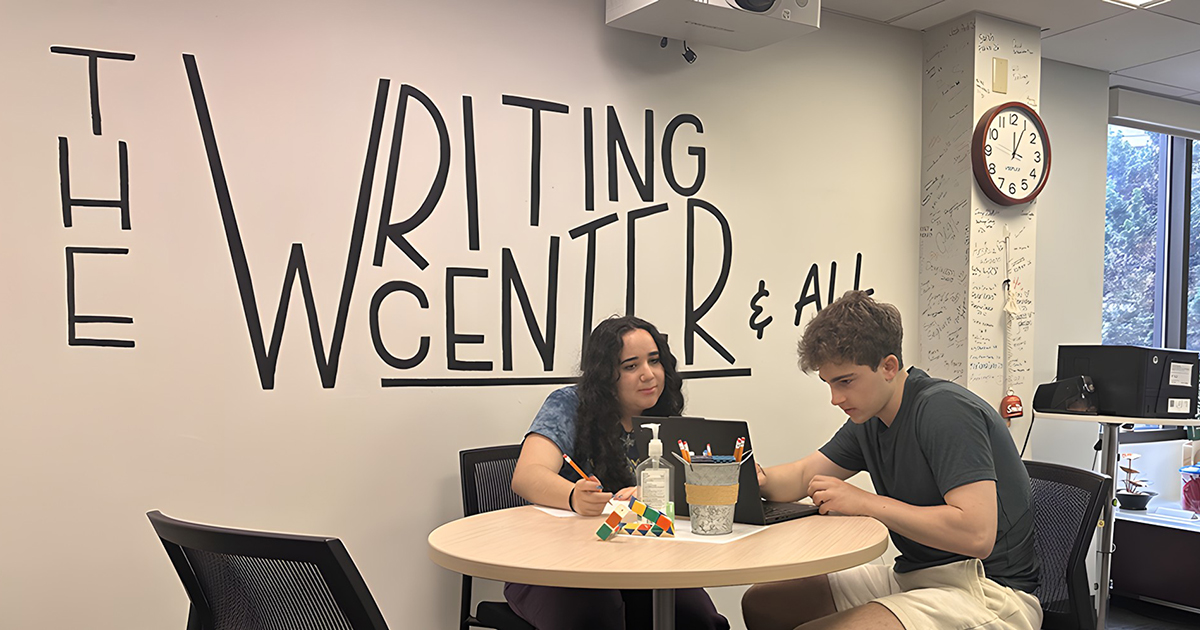 A young woman and man converse while sitting at a table in Babson's writing center.